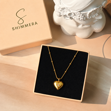 Gold heart-shaped necklace in a Shimmera box with a decorative vase in the background.