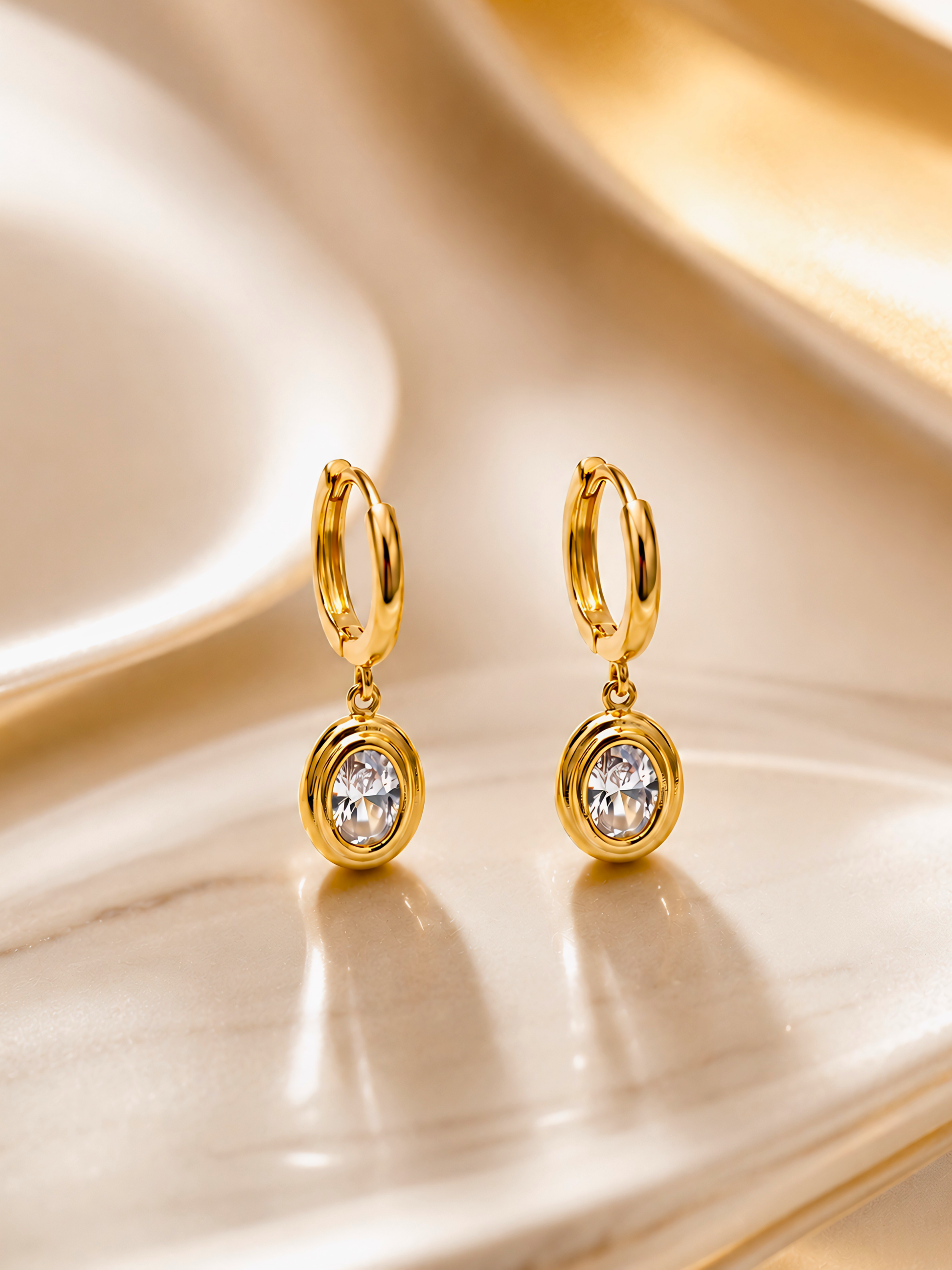 Gold hoop earrings with clear gemstones on a reflective gold surface