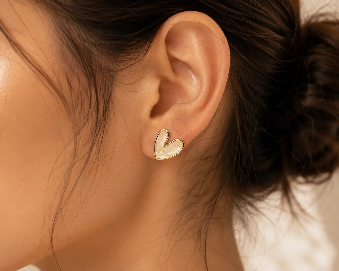 Close-up of an ear wearing a heart-shaped gold earring with blurred hair and background