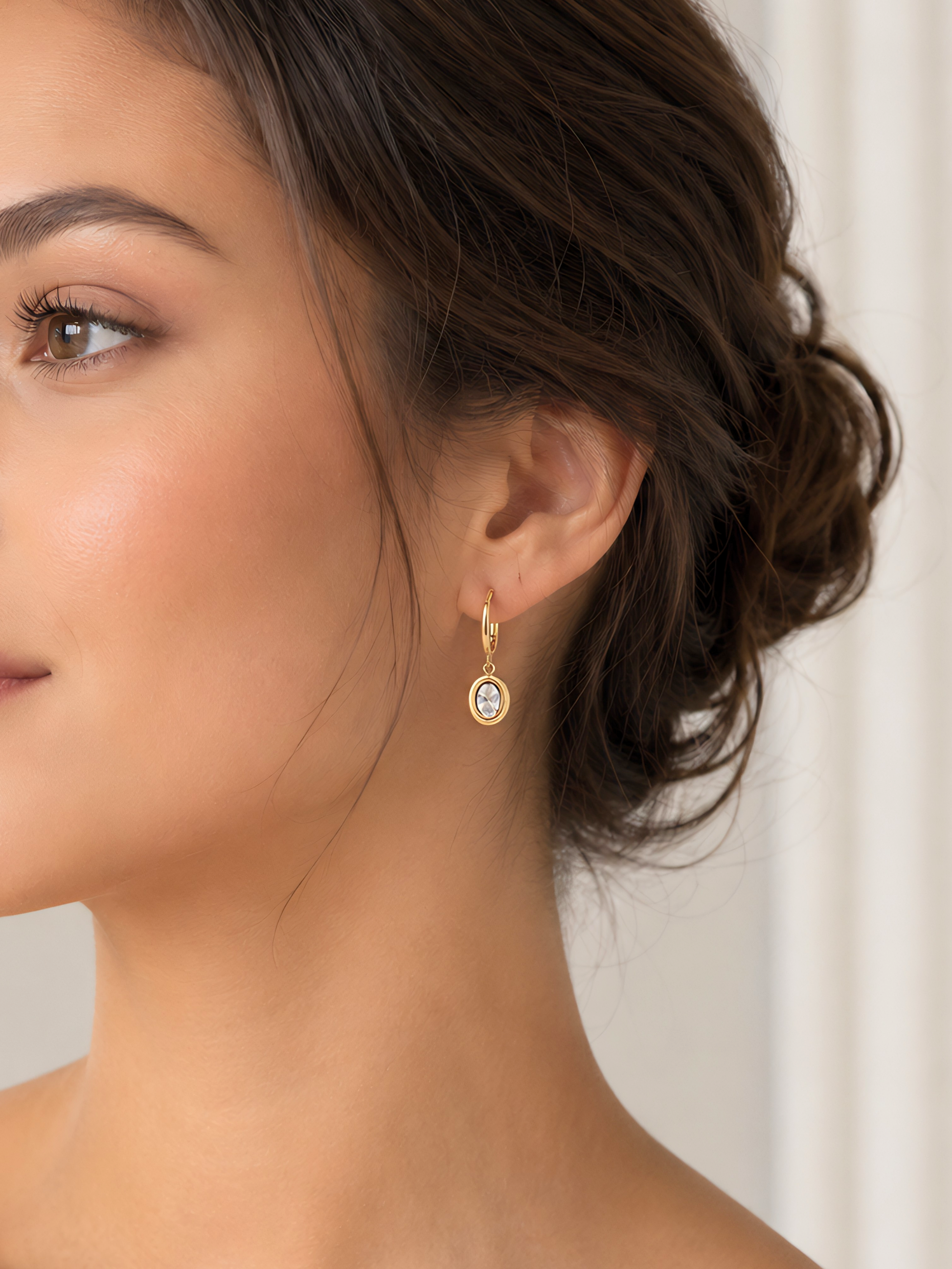 Close-up of a woman wearing gold earrings with a white stone.