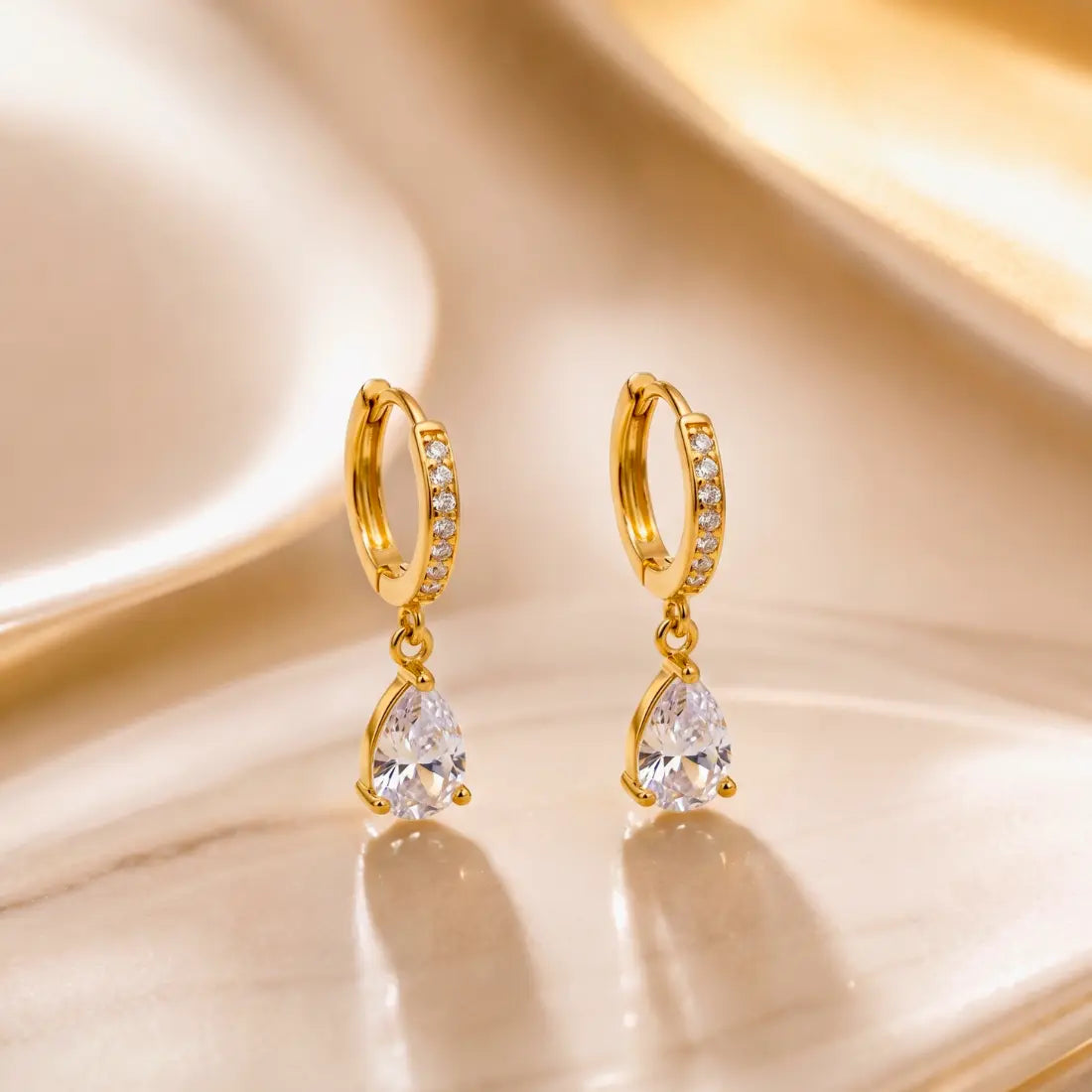 Gold hoop earrings with teardrop-shaped gemstones on a reflective gold surface