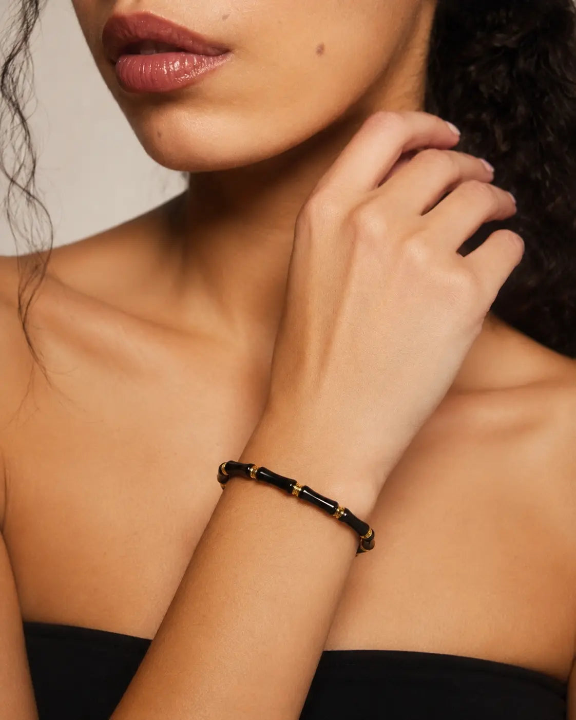 Close-up of a woman's arm wearing a black and gold bracelet against a neutral background