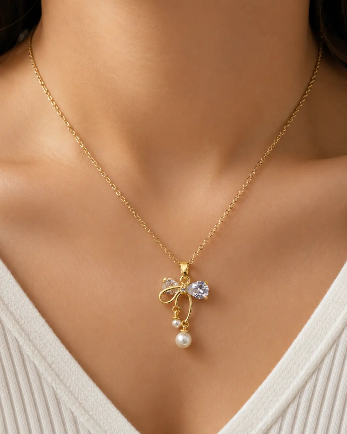 Gold necklace with a bow and pearl pendant on a model wearing a white top.