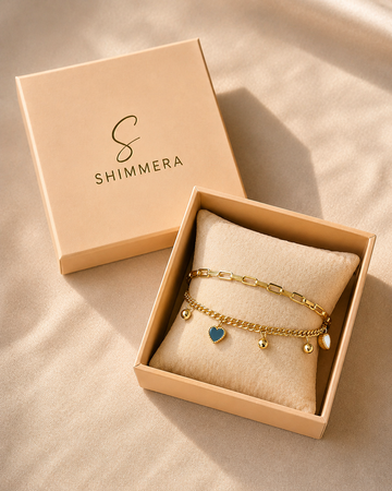 Gold bracelet with heart charm in a 'Shimmera' box on a beige background